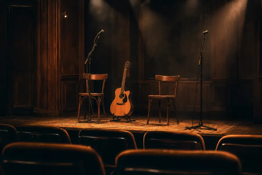 An empty theatre stage set with a guitar, chairs and microphones