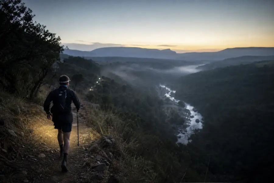 A trail runner with a headlamp above a river gorge before dawn